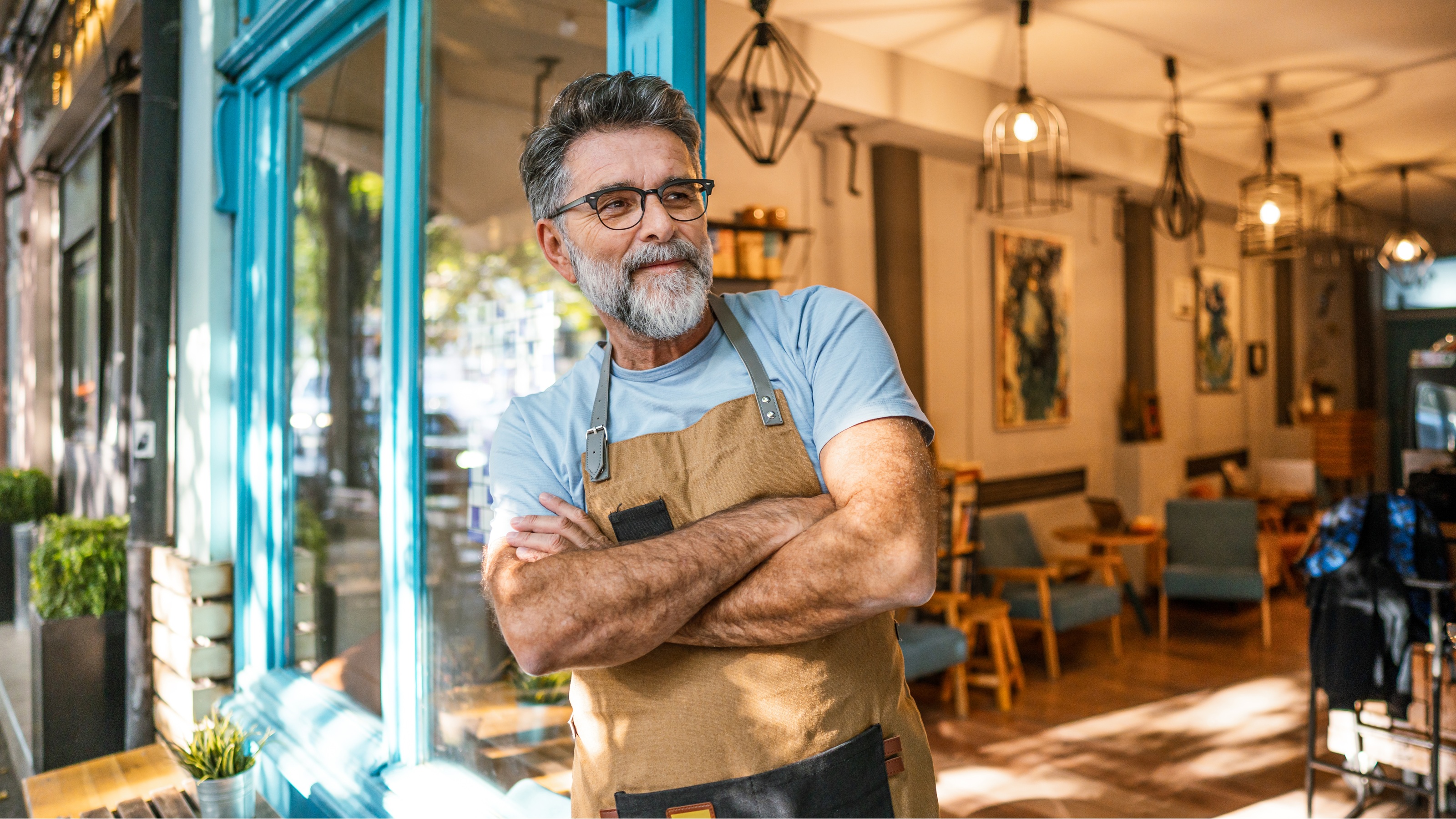 An older business owner stands outside his coffee shop, ready for customers.