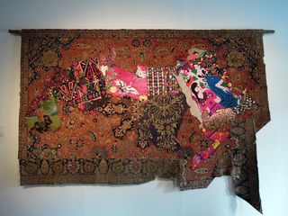 View of 'Arab Spring Map' by Bokja Design - a distressed red, black and brown antique rug with a bright coloured map design in the centre hanging on a wall