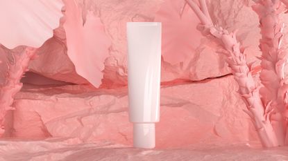 Make-up cosmetic tube in front of pink backdrop of crumbled powders