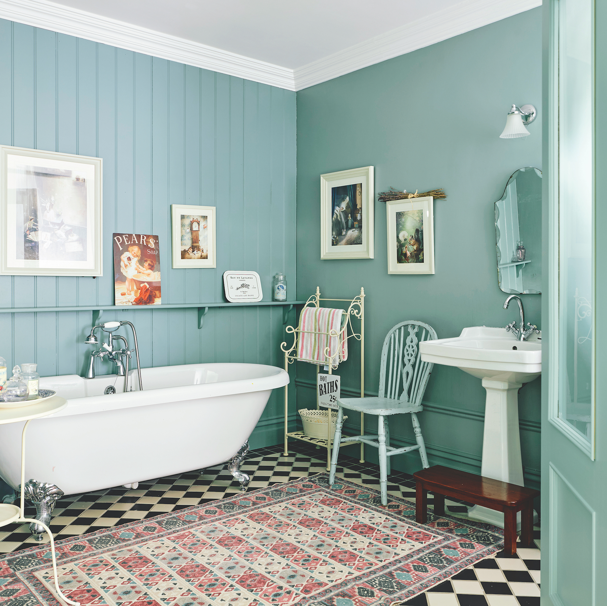 bathroom with wood panel walls painted blue and white roll top bath with vintage rug on top of black and white tiles