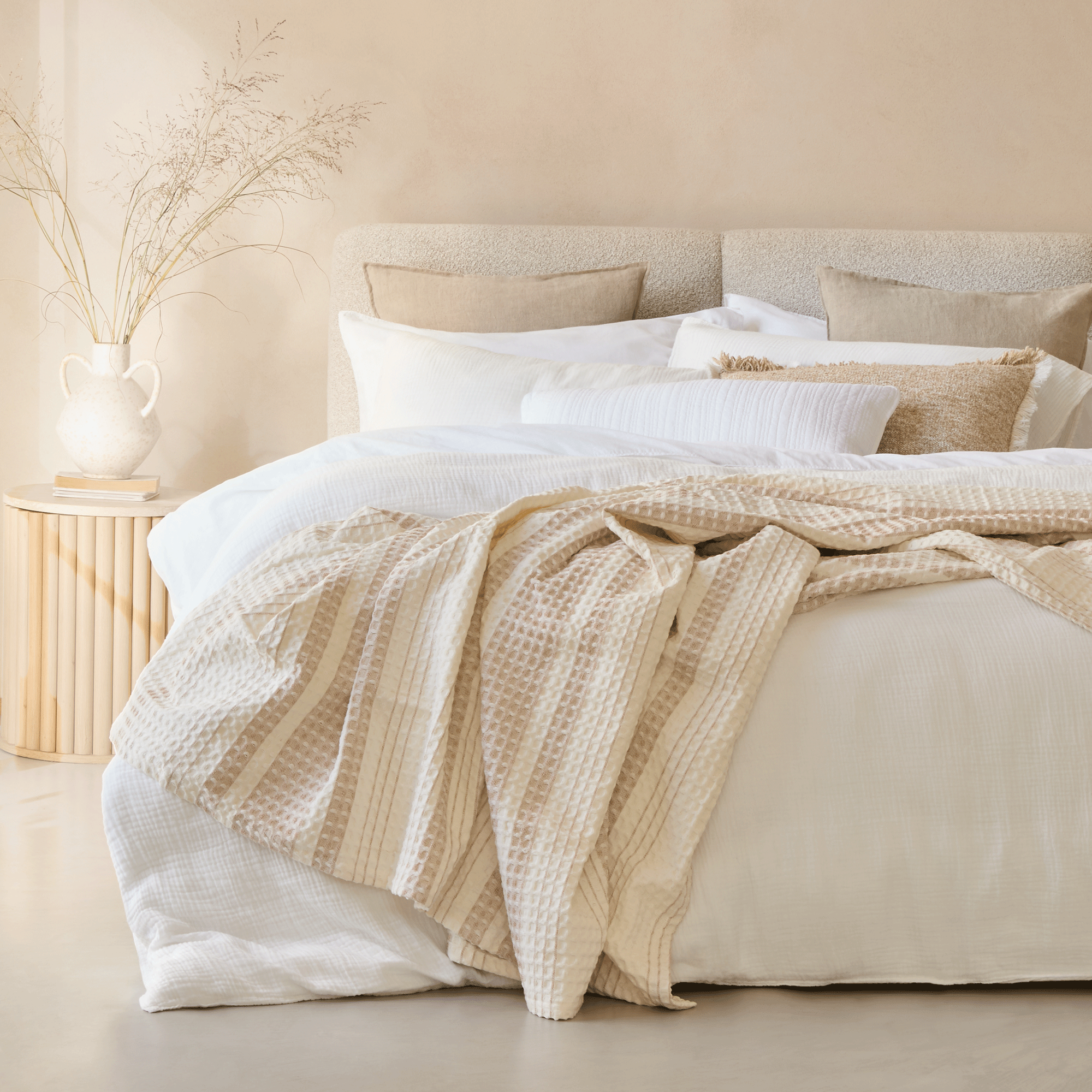 a neutral bedroom with a bed layered in crisp white bedlinen and textured throws and pillows