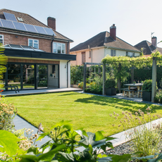A neat, green lawn bordered by a pergola and flower beds.