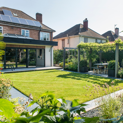 A neat, green lawn bordered by a pergola and flower beds.