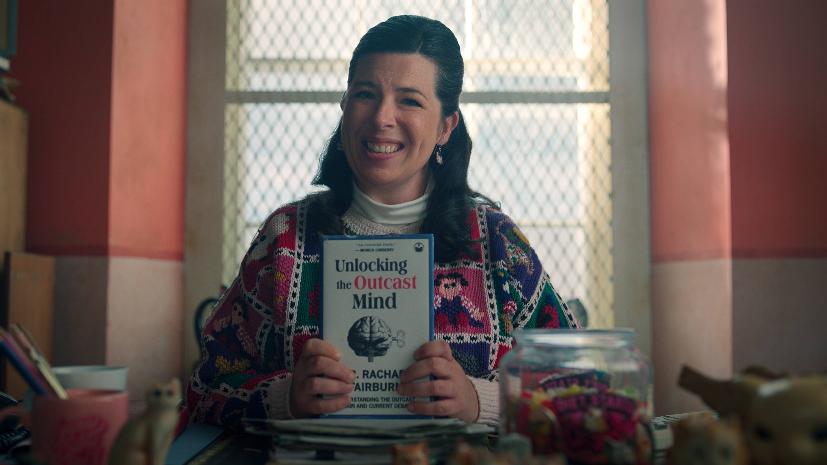 Heather Matarazzo as Judi Spannegel holding up a book in Wednesday season 2