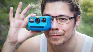 Photographer James Artaius holding a Blue Polaroid Go Gen 2 camera, in a woodland setting