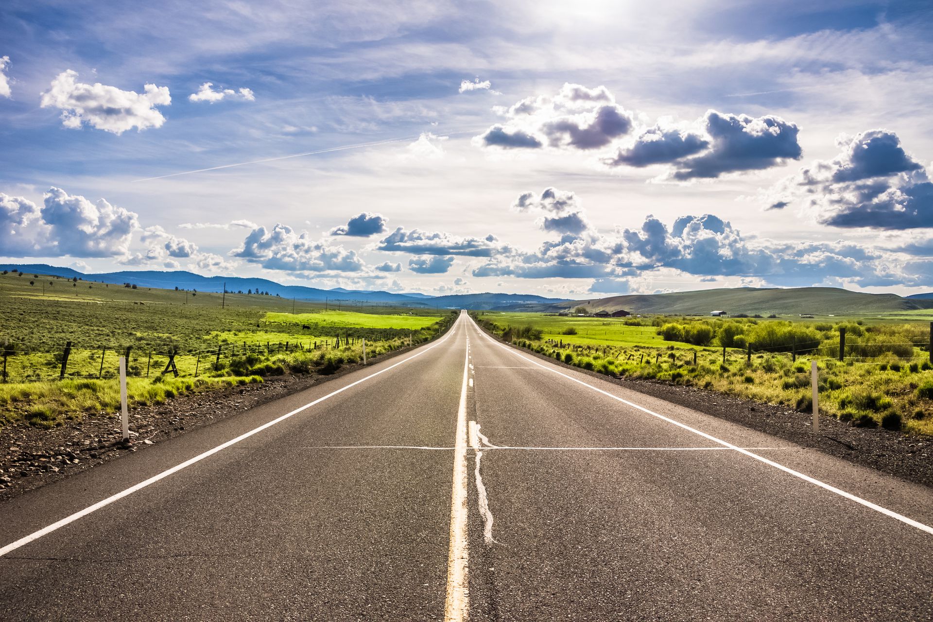 road leading to the Umatilla National Forest with grass on either side and mountains in the distance