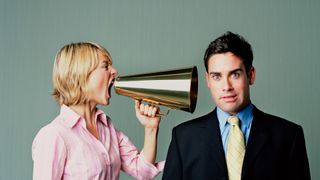 Female office worker shouting in a colleague's ear using a megaphone.