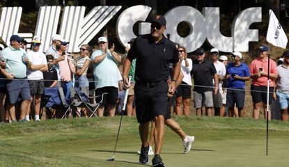 Mickelson walks on the putting green, in front of an LIV Golf banner