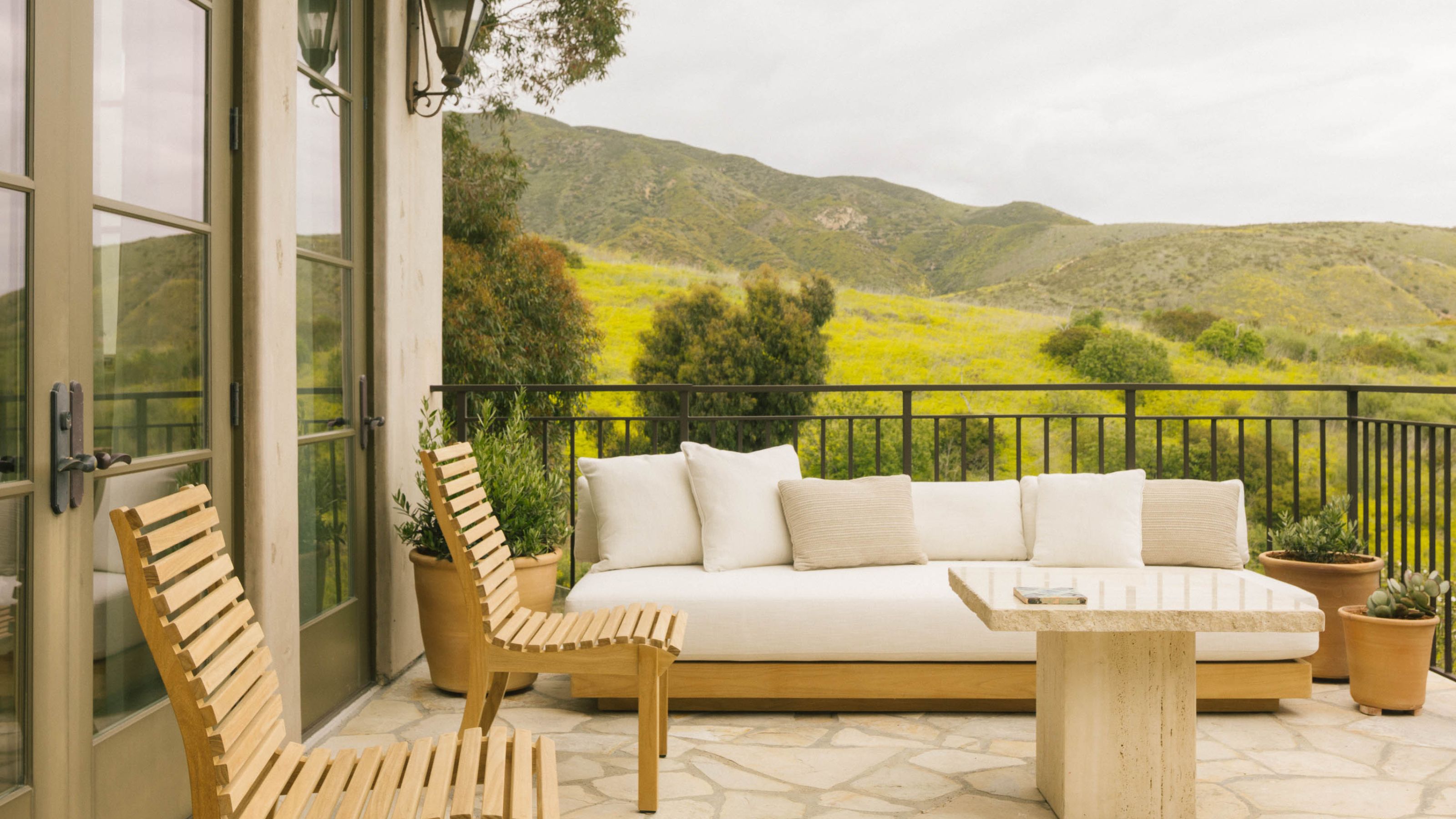 a raised terrace overlooking hills in Malibu with light wooden furniture and potted plants