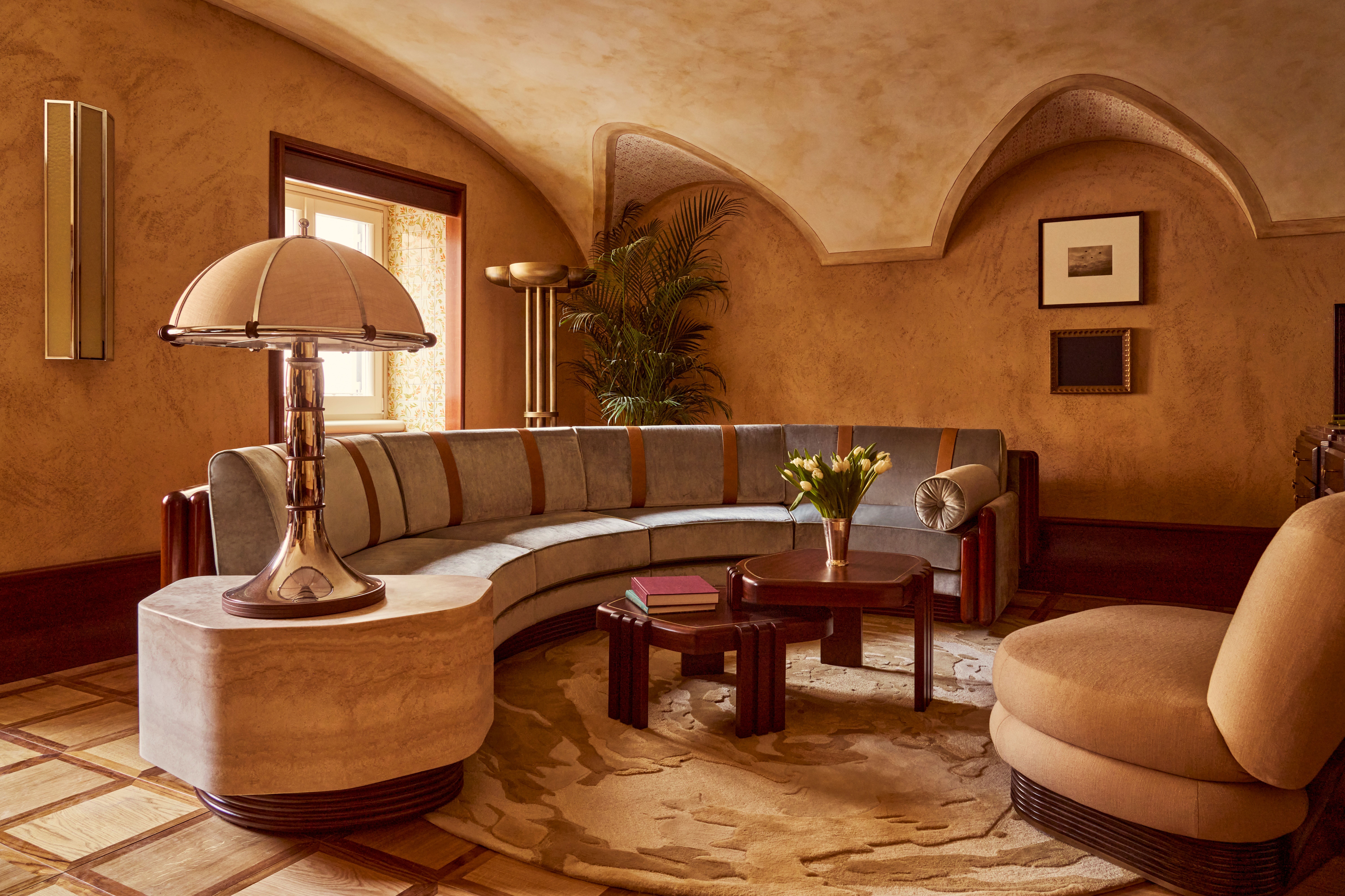 The interiors of a palatial hotel housed inside a 16th-century building with frescoed walls, textural arches, mesmerizing flooring, and plenty of wood oozes antique-inspired furniture and a golden atmosphere across sculptural furnishings, artworks, and plants.