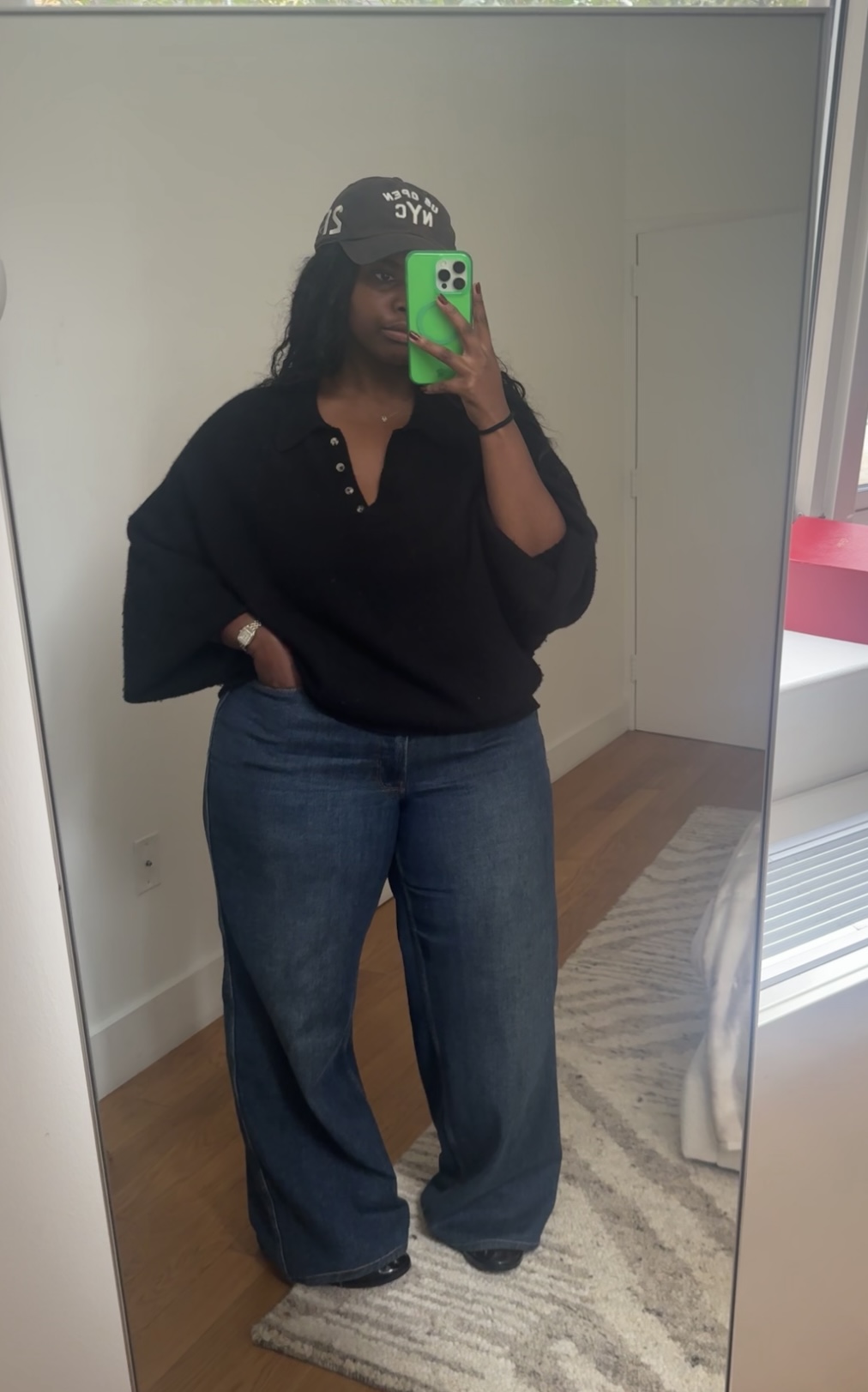Tariro Makoni wearing a black sweater and jeans while taking a mirror selfie