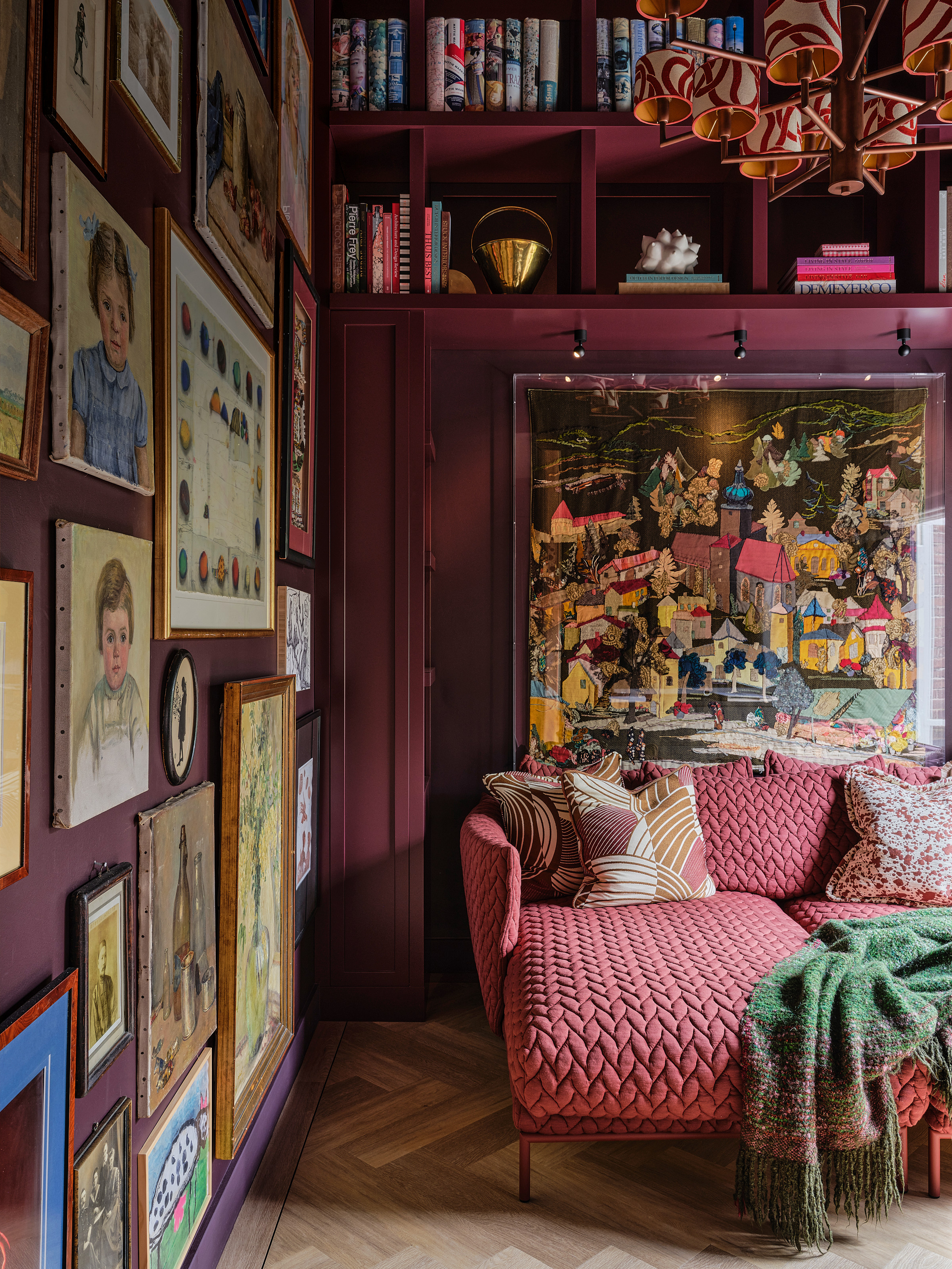 Snug with deep purple walls, patterned pink chaise longue sofa, and artwork all over the wall