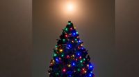 a bright ball of light illuminates the sky above a cone-shaped evergreen tree covered in colored light bulbs