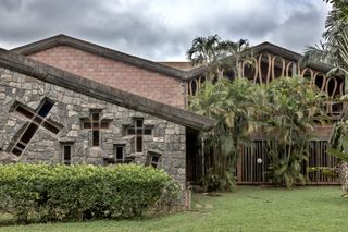 Daytime exterior image of the Dominican Institute’s lounge and refectory feature stone, brick and sand-casted screen walls, green lawn and hedges, trees, cloudy sky