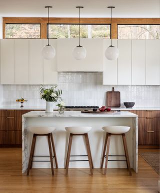 timeless interior design styles, white and wood mid century style kitchen, pearlescent wall tiles, modern white wall cabinetry, marble island, modern mid century stools, trio of white globe pendants