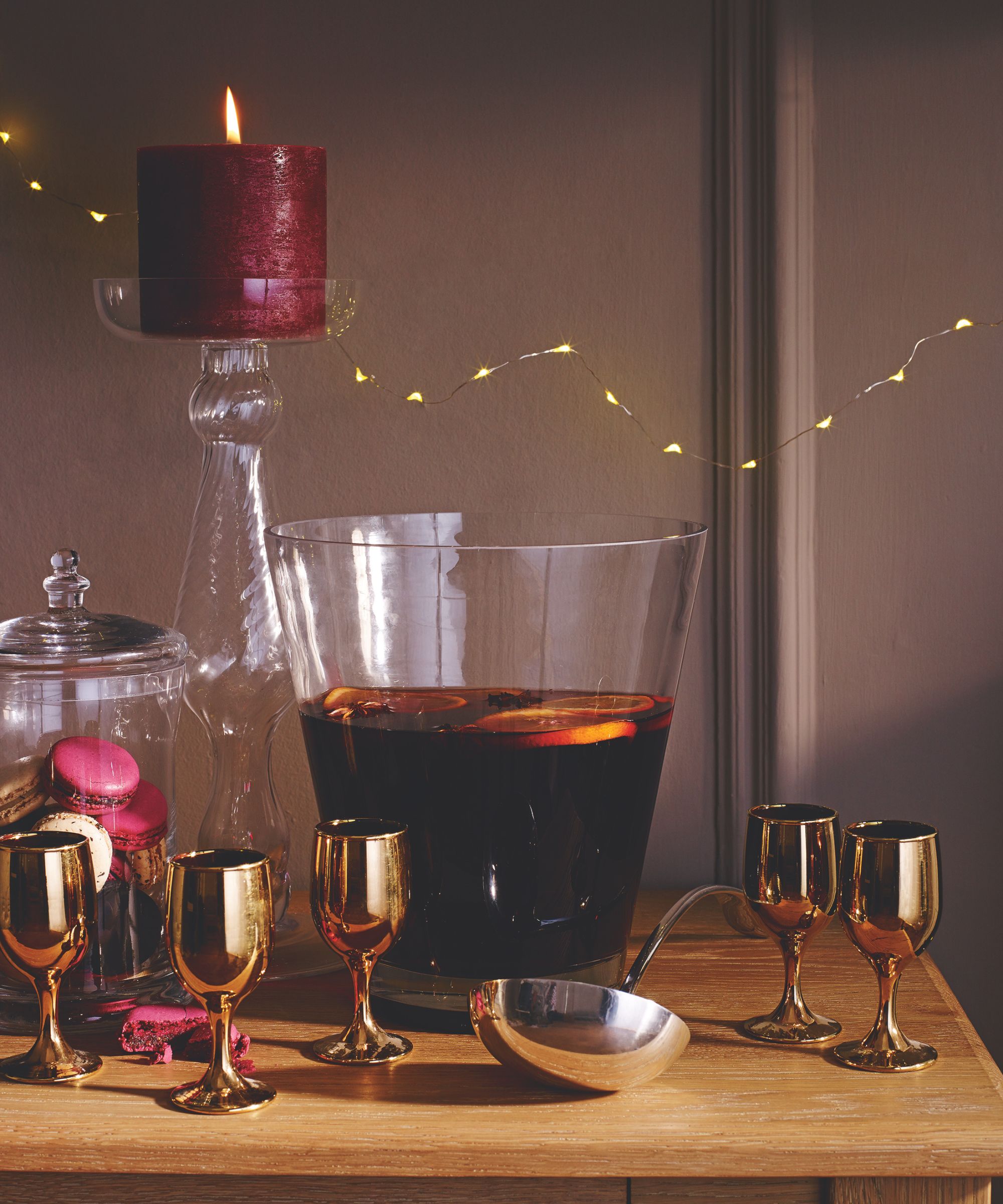 Wood table with glass punch bowl filled with mulled wine, and gold wine glasses beside