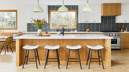 A kitchen with a white oak island and white quartz worktop, black and white bar stools and black backsplash tiling