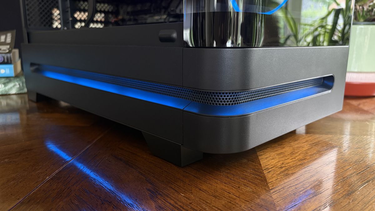 A close-up of a black Nitro 65 computer case with a blue LED strip along the bottom, showing a transparent cooling reservoir on the side, set on a wooden surface.