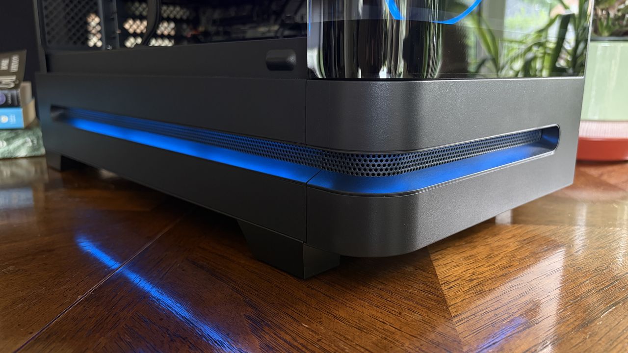 A close-up of a black Nitro 65 computer case with a blue LED strip along the bottom, showing a transparent cooling reservoir on the side, set on a wooden surface.