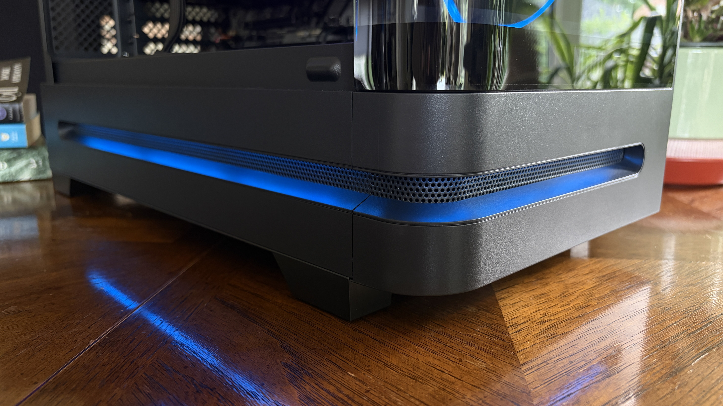 A close-up of a black Nitro 65 computer case with a blue LED strip along the bottom, showing a transparent cooling reservoir on the side, set on a wooden surface.