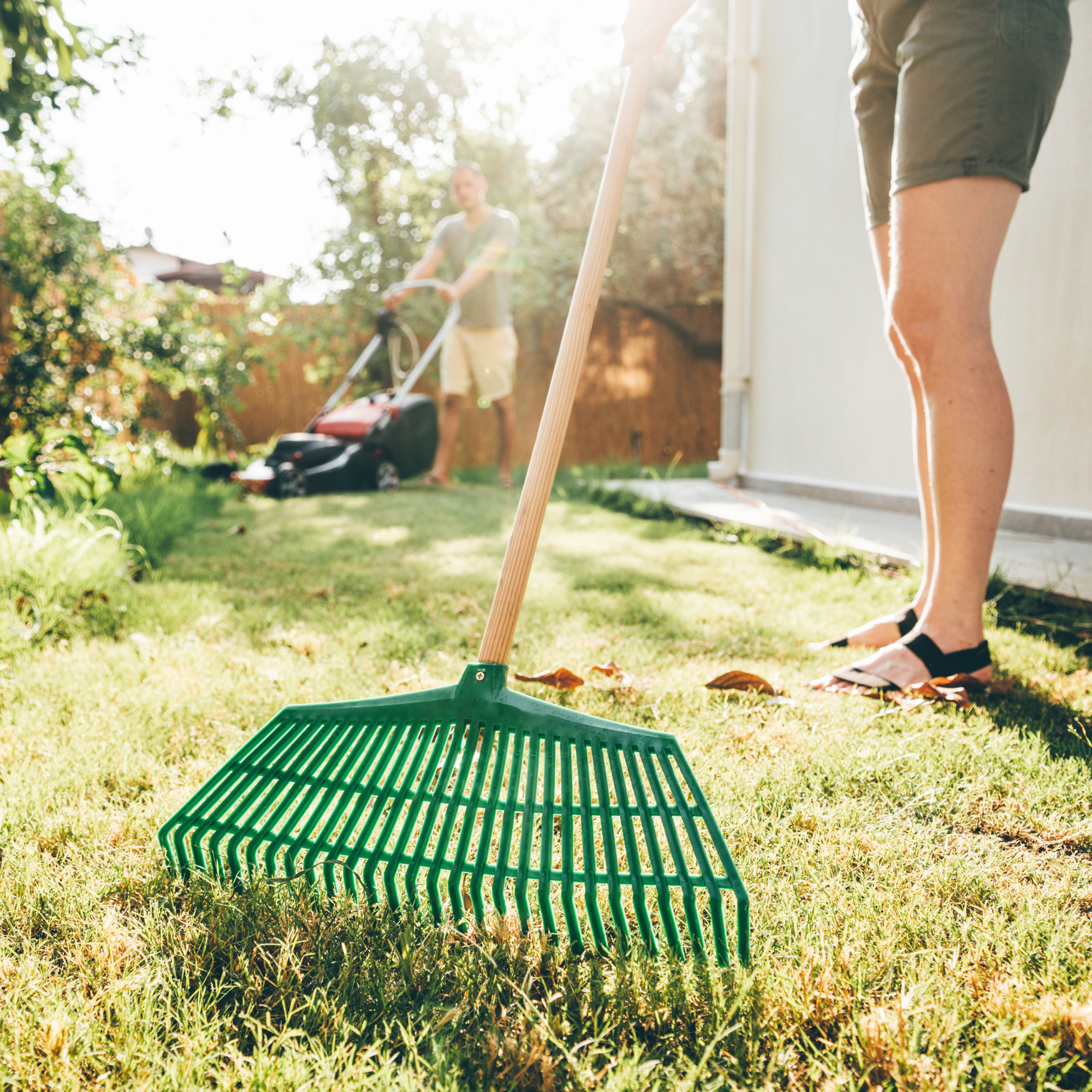 man and woman doing spring lawn care with rake and lawnmower