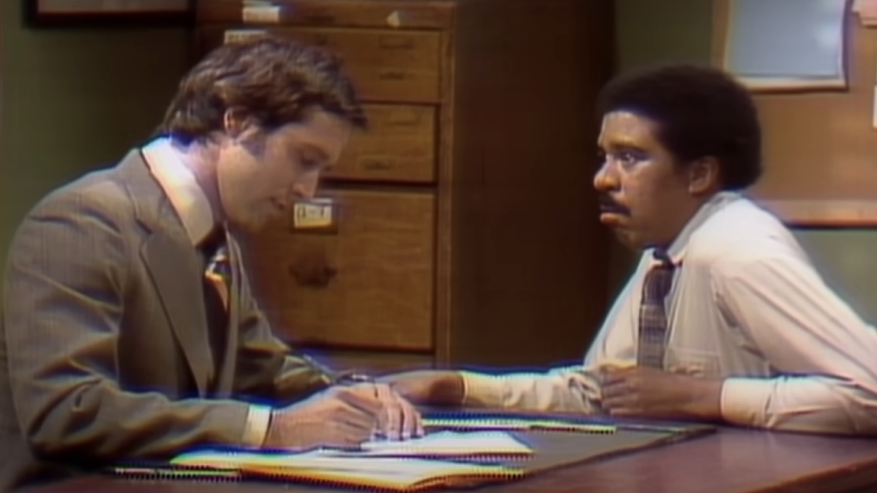 Chevy Chase sitting opposite Richard Pryor on Saturday Night Live