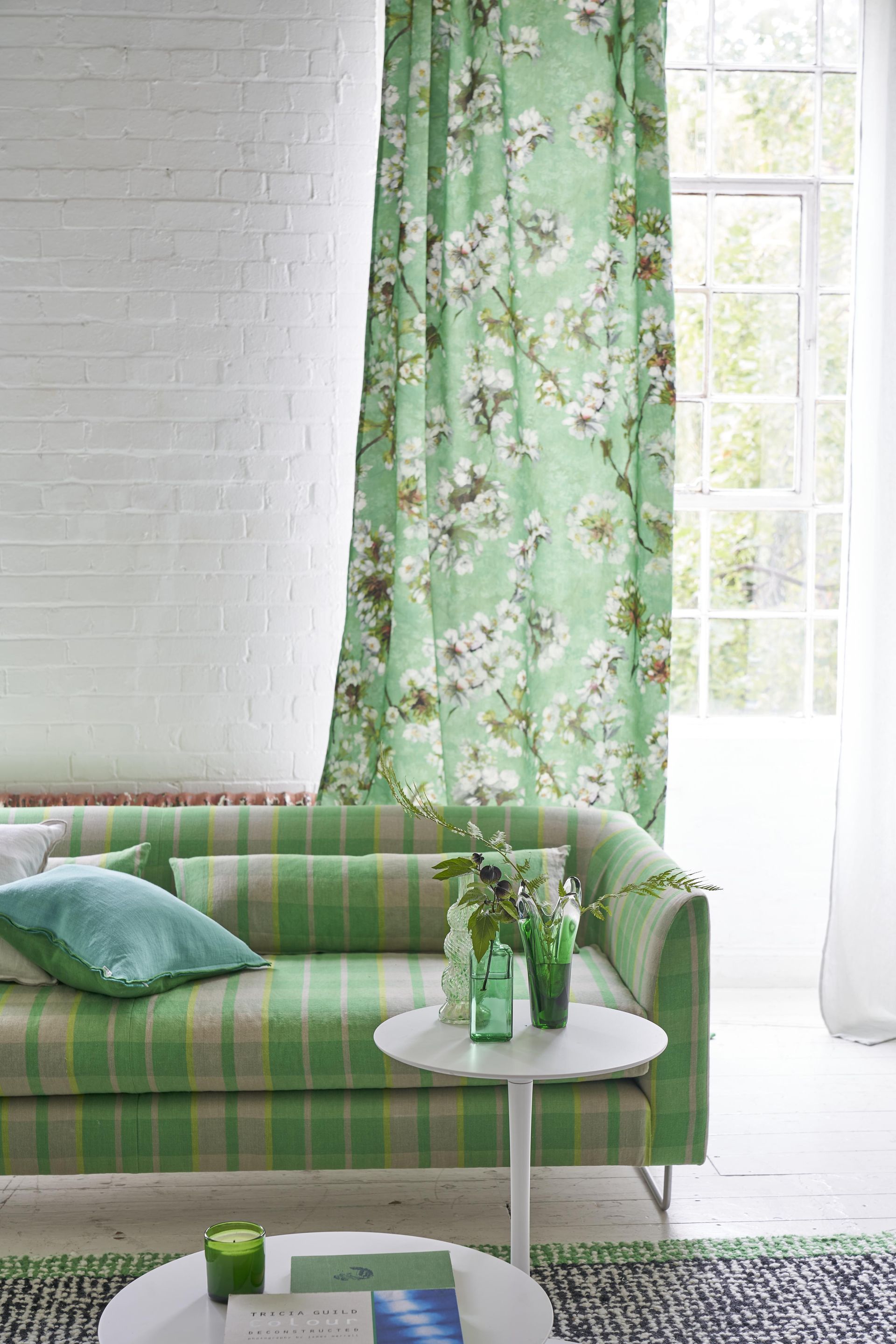 white and green living room with green floral drape, green check couch, side table, black and green rug