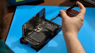 Un hombre realiza una reparación de autoservicio de Apple en un iPhone que descansa sobre una alfombrilla azul