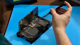 A man doing an Apple Self Service Repair on an iPhone resting on a blue mat