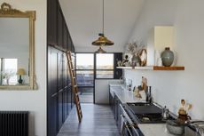 modern country style kitchen with black cabinetry, open shelving, brass pendants, ladder to storage, ornate mirror, crittall window