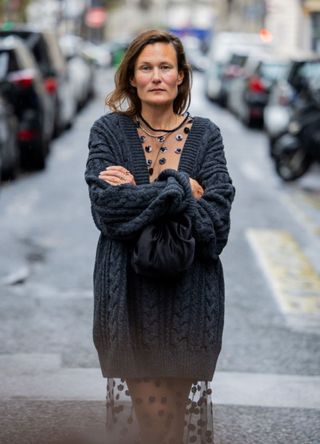 A woman wearing a mesh dress with sequin embellishments underneath a cable knit jumper