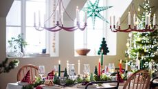 Image of a white dining room decorated for Christmas. There is a table full of decor and two red candle chandeliers hanging over it.