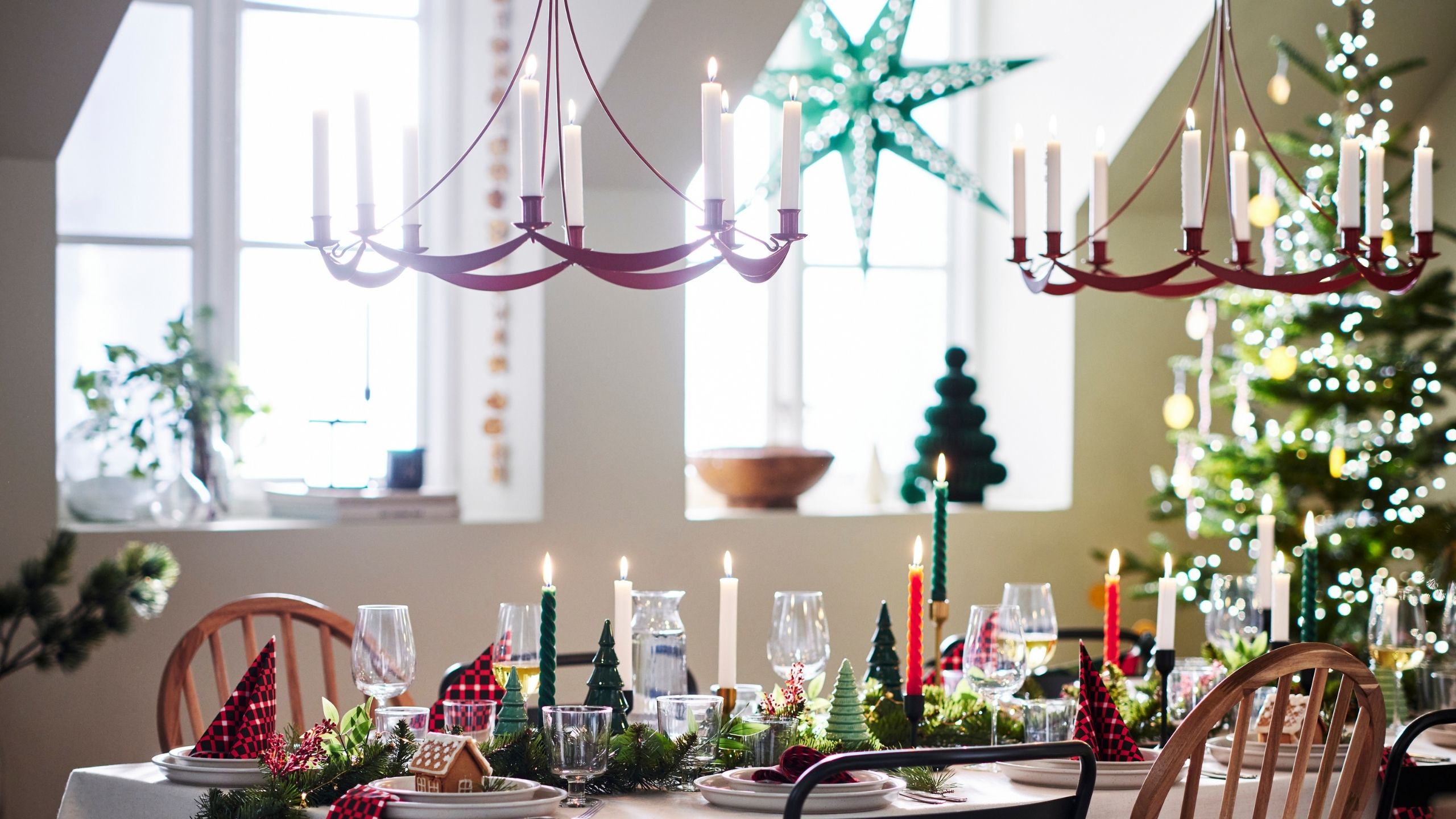 Image of a white dining room decorated for Christmas. There is a table full of decor and two red candle chandeliers hanging over it.