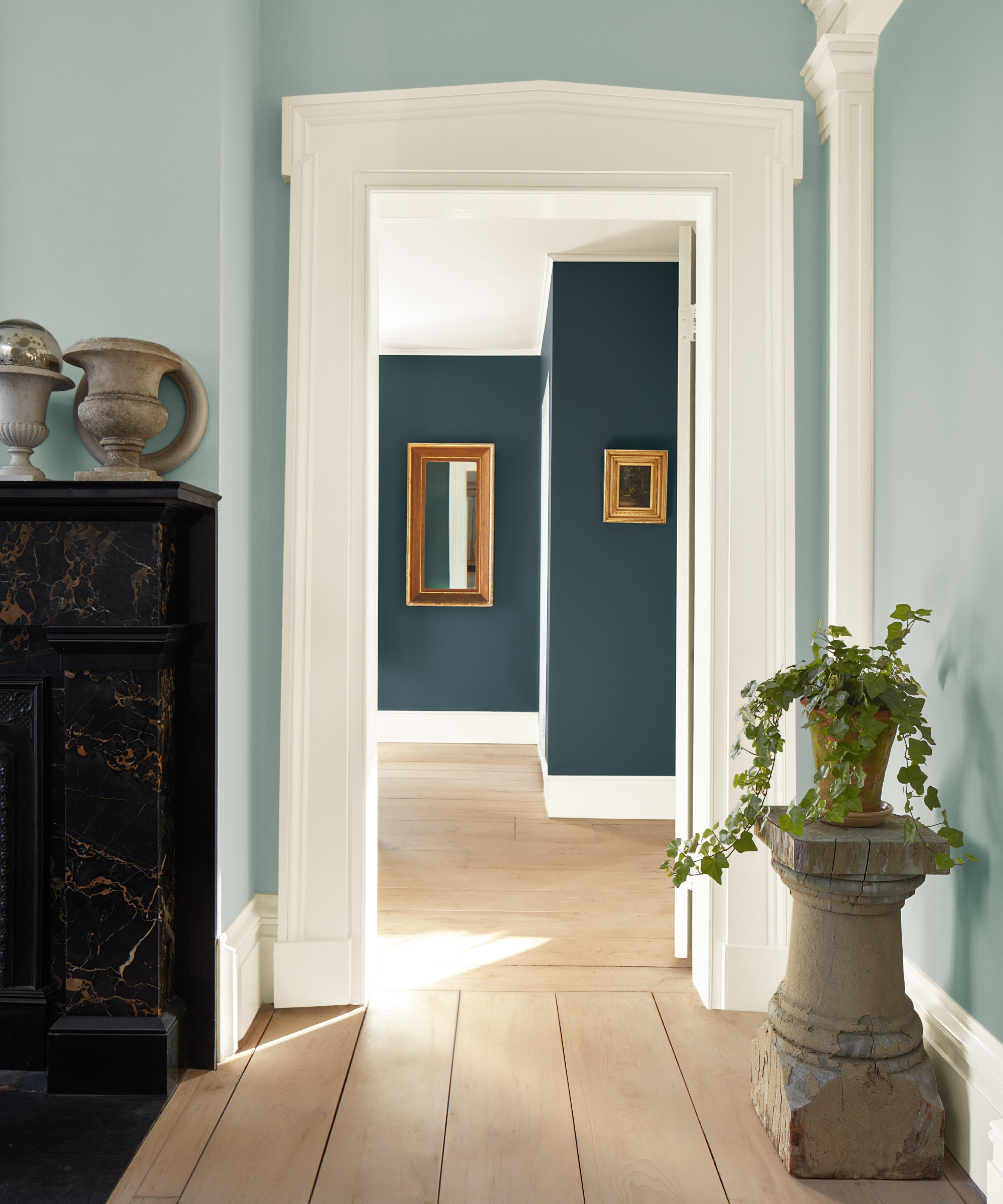 room and doorway with walls in pale blue, woodwork in white leading to another room with darker blue walls