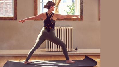 Woman doing Pilates for strength training at home on yoga mat, in front of open window