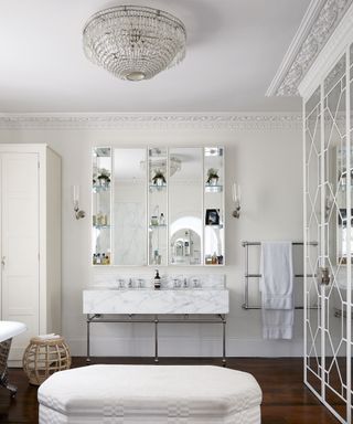 A white bathroom with a chandelier and white ottoman