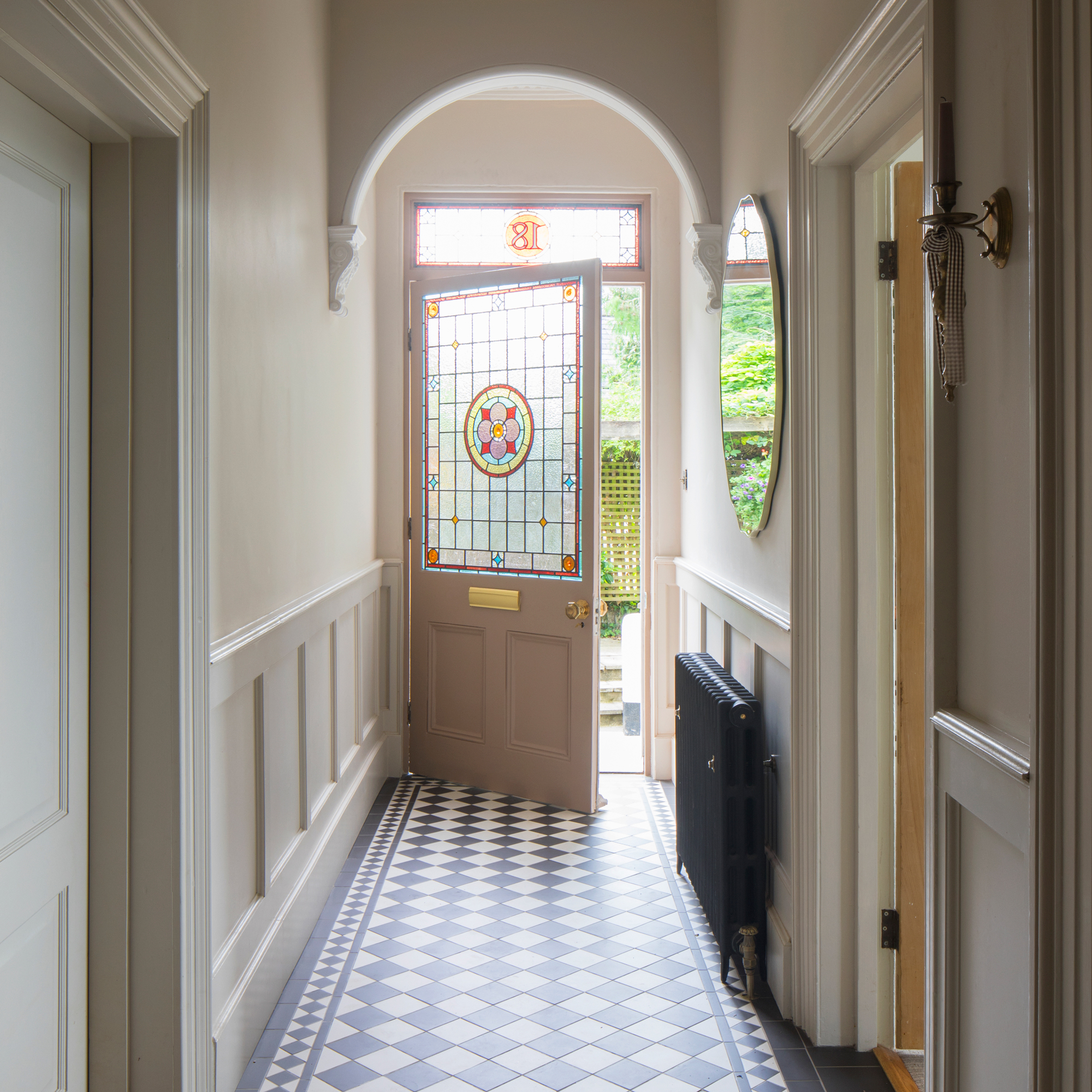 a classic monochrome tiled hallway leading to a stained glass door