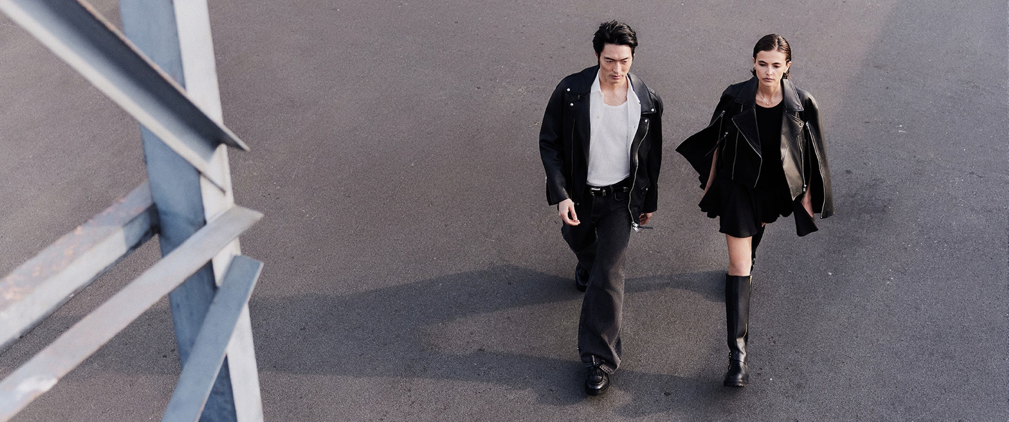 A male and female model from birds eye view wlaking down a road wearing outfits and jackets sold at AllSaints