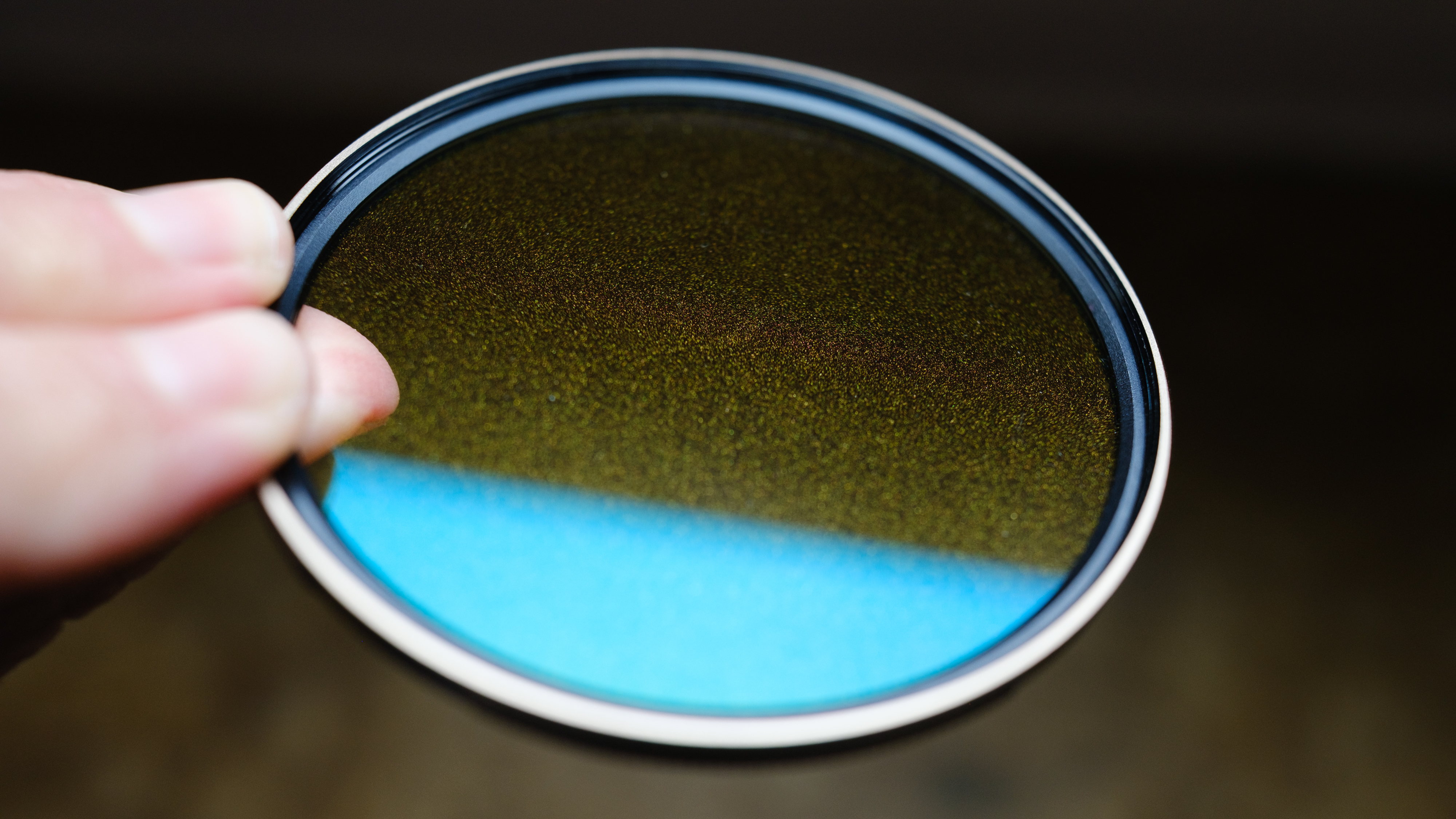 The Polar Pro McKinnon 135 Gold Mist filter in a person's hands with a window reflection