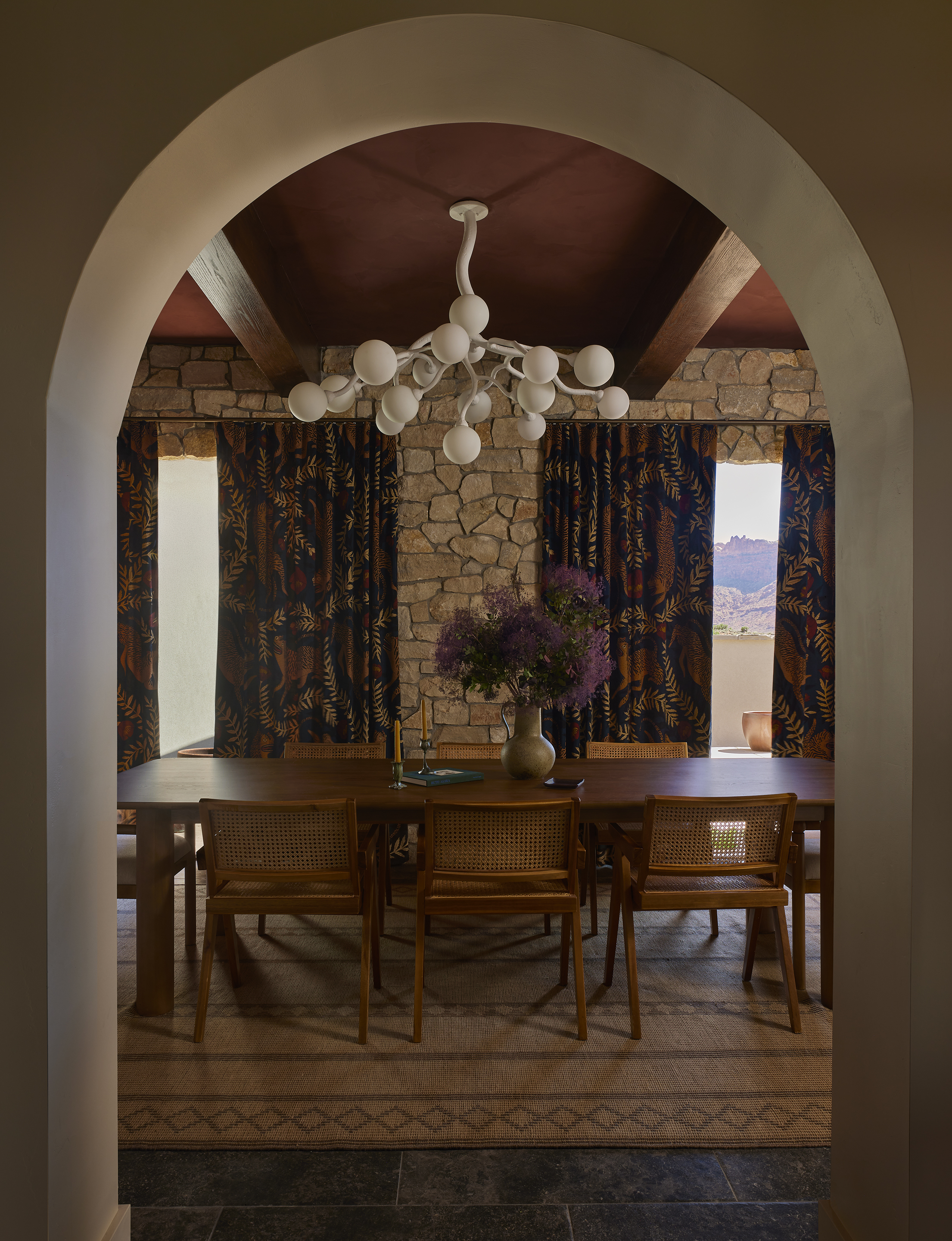 dining room through an arched entrance with a branch-like chandelier hanging over a wooden dining table