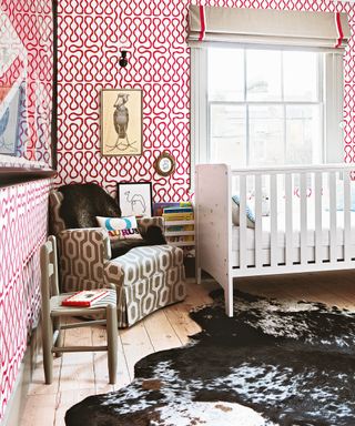 Gender neutral nursery ideas featuring red and white wallpaper, a white painted crib and brown armchair.