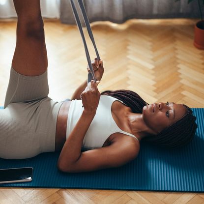 A woman doing a resistance band leg workout at home on a workout mat