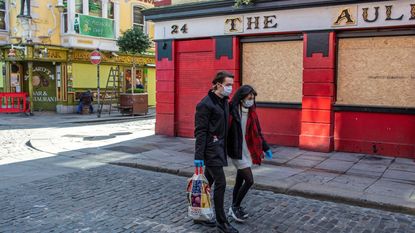 A couple wearing face masks carry a shopping bag as they pass a temporarily closed pub in Dublin.