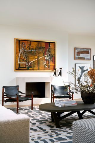 White living room with dark wood furniture, artwork above fireplace and gallery wall in alcove to the right