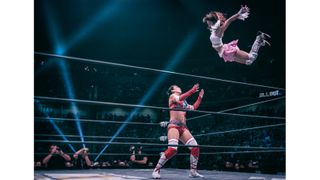 One female wrestler jumping on another in the ring