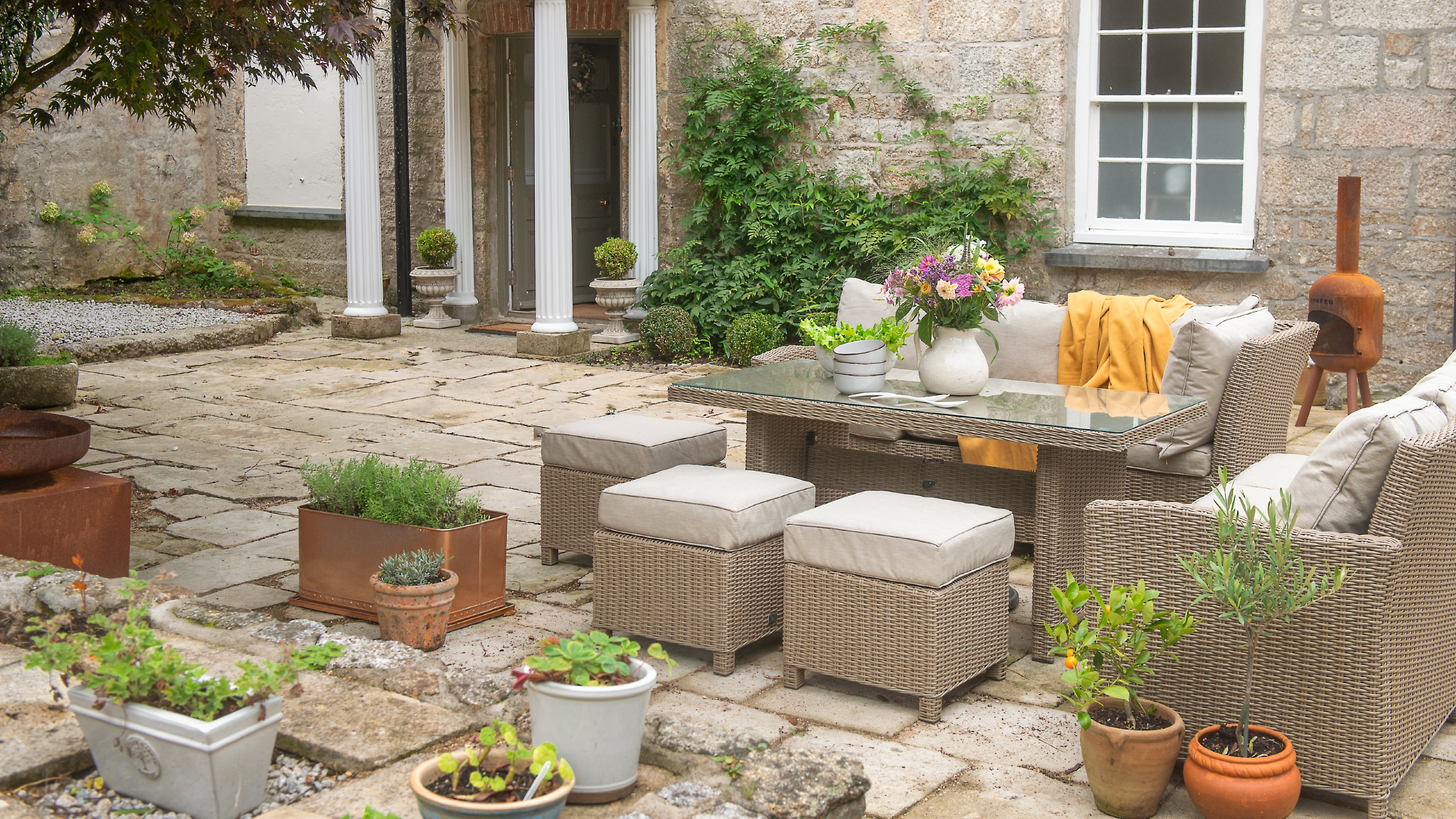 A patio with a rattan garden lounge set with cream cushions surrounded by terracotta plant pots 