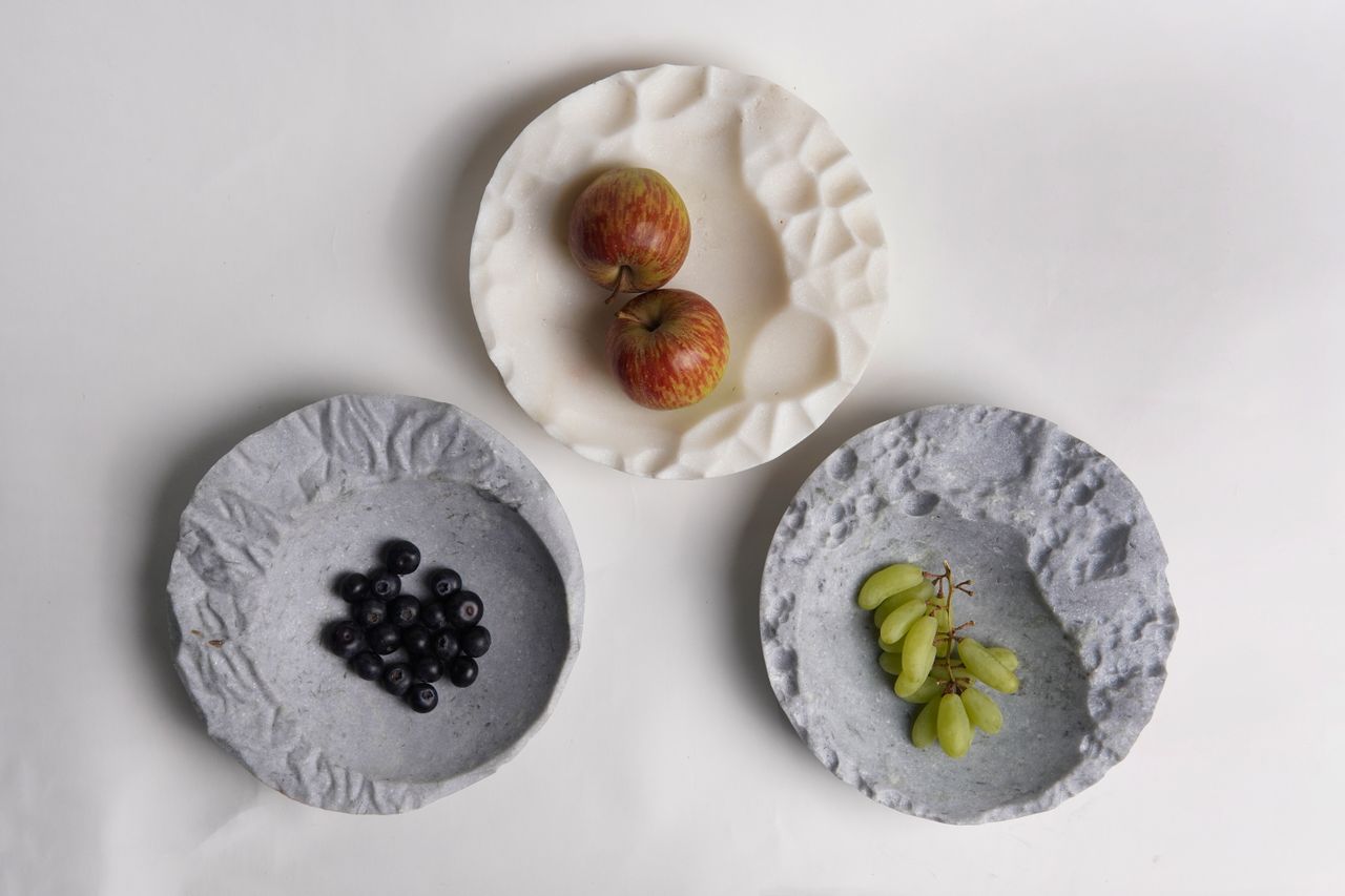 Two plates in grey contain multiple, colorful fruits and are photographed against a neutral background.