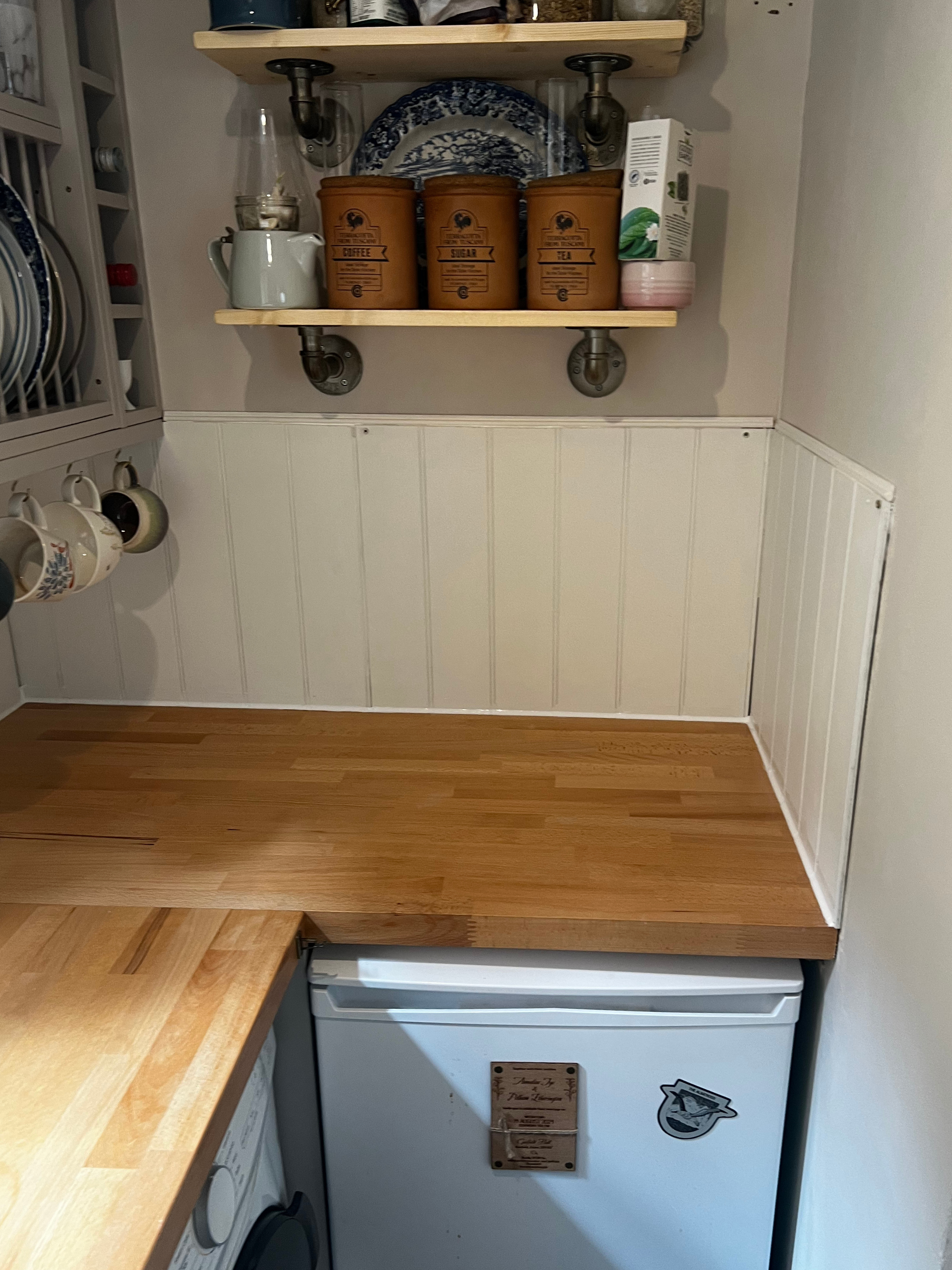 A kitchen with bare wooden countertops and white tongue and groove panelling