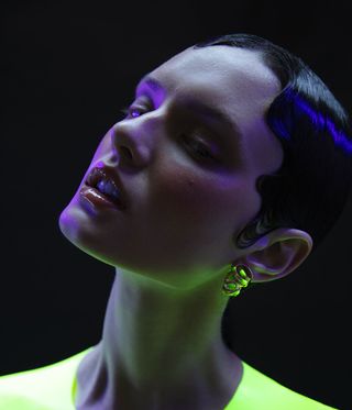 Woman wearing gold-coated brass earrings with florescent yellow dots on