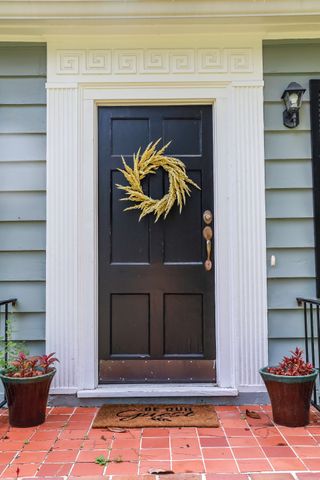 a black front door and a wreath on a revently renovated blue small cottage style house with brick steps